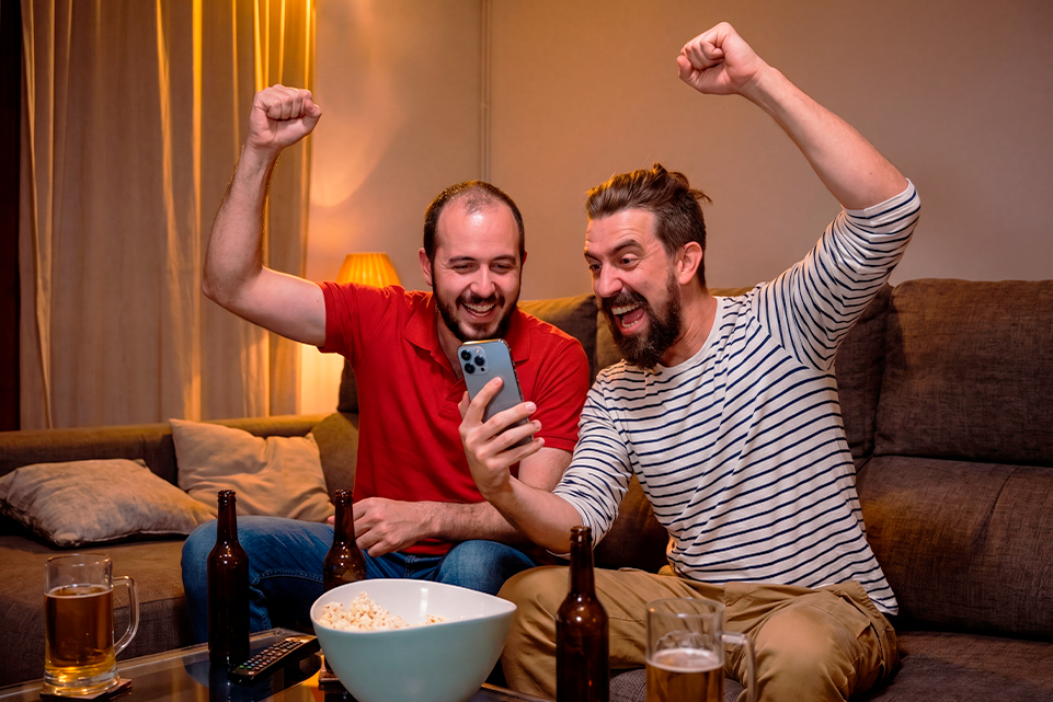Dos aficionados celebrando frente al celular mientras siguen el Progol eliminatorias en casa.