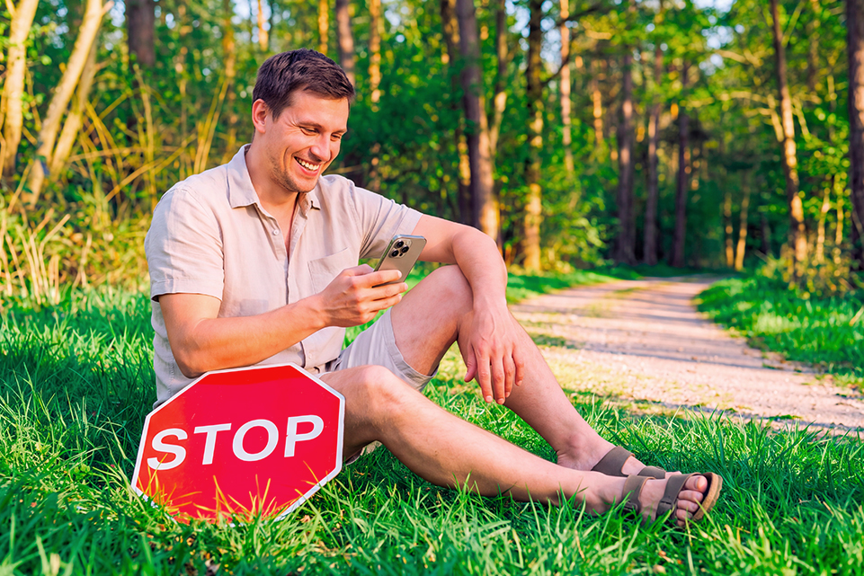Hombre mirando su celular junto a una señal de STOP, imagen sobre errores al jugar la lotería.