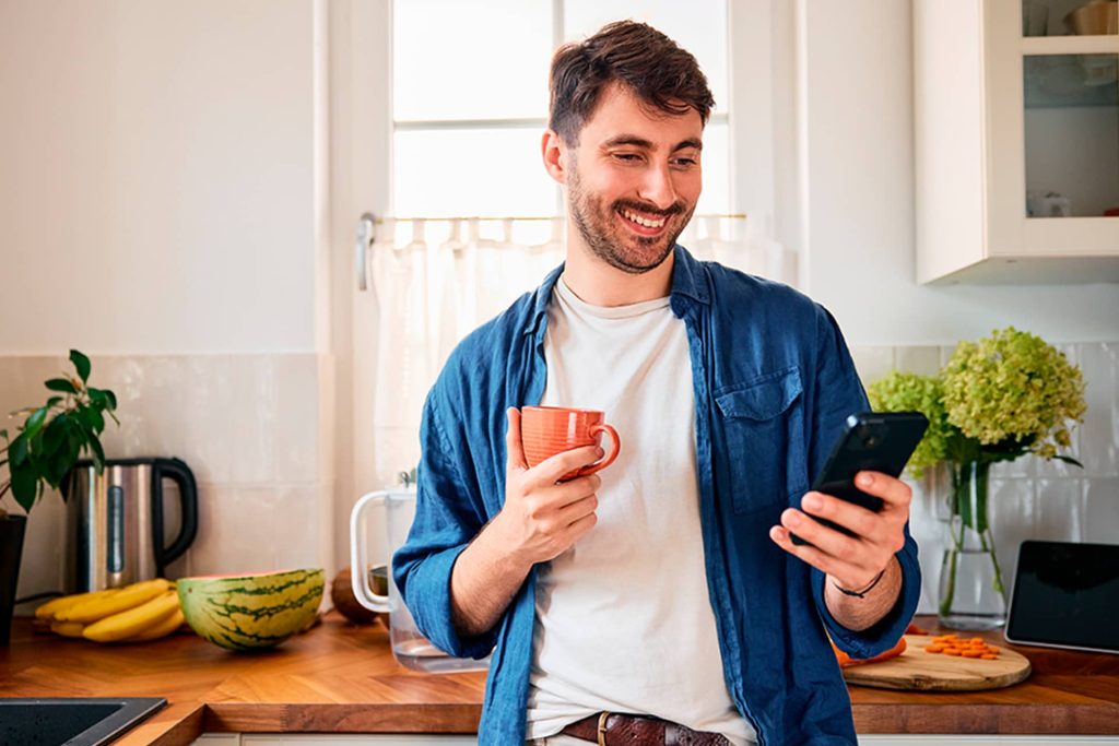 Hombre con una taza mirando su celular en la cocina, imagen para una guía sobre cómo elegir números de Melate.